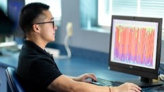 Researcher works at a computer analyzing colorful data visualizations in a medical or scientific lab setting.