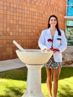 Gabriela Rajic stands in her white coat next to the pestle and mortar pharmacy statue