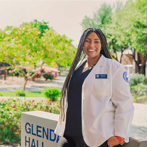 Student posing on campus in white coat