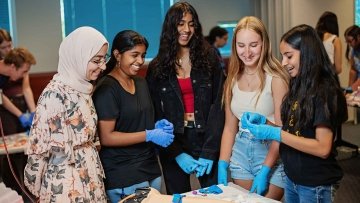 Five students wearing latex gloves learn about anatomy with a dummy arm