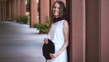 AnnaLisa West (SLP '26) stands with her graduation cap and masters hood on campus