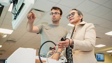 A podiatry student points to a screen while a summit participant learns to use a surgery simulator.
