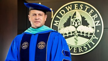 Dr. Joshua C. Baker, President and CEO of Midwestern University, in his academic regalia next to the Midwestern University seal.