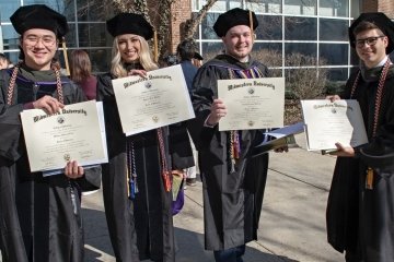 Four College of Pharmacy graduates holding their diplomas.
