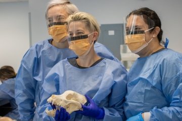 Three people in medical protective gear. One holding animal skull