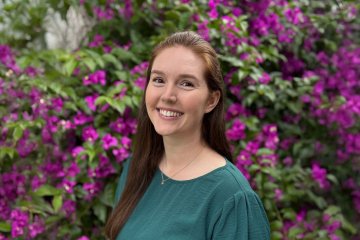 Jenna Hoover smiles at the camera in front of purple-flowered bushes