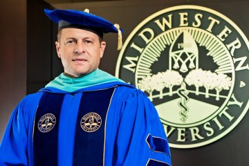 Dr. Joshua C. Baker, President and CEO of Midwestern University, in his academic regalia next to the Midwestern University seal.