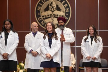 Students in the College of Health Sciences - Illinois receive their white coats on stage