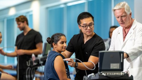 Medical student performs an ultrasound on a woman’s shoulder while a physician observes and reviews the monitor in a clinical lab setting.