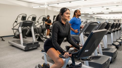 A woman on a stationary bike and a man on a treadmill exercise in a modern campus fitness center.