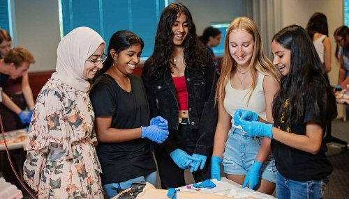 Five students wearing latex gloves learn about anatomy with a dummy arm
