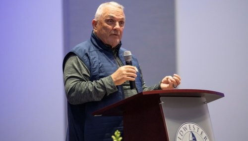 Rudy Ruettiger delivers a speech at a podium during an evening event.