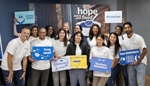 Group of volunteers in white shirts holding fun signs at a food drive event with the slogan “hope starts with food” in the background.