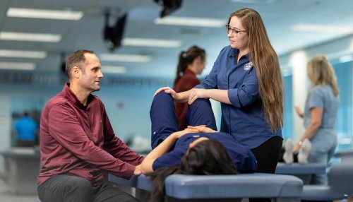 A student makes an osteopathic adjustment on a student patient while a professor gives instructions.