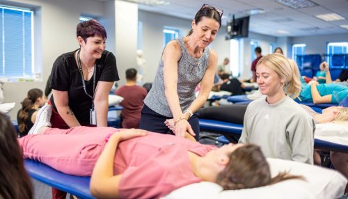 Faculty member demonstrates physical therapy to students in lab.