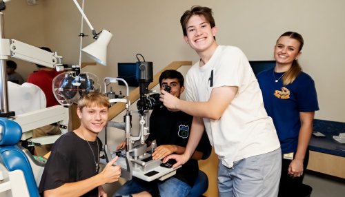 Students explore an optometry exam room, taking turns using a slit lamp during a hands-on learning experience.