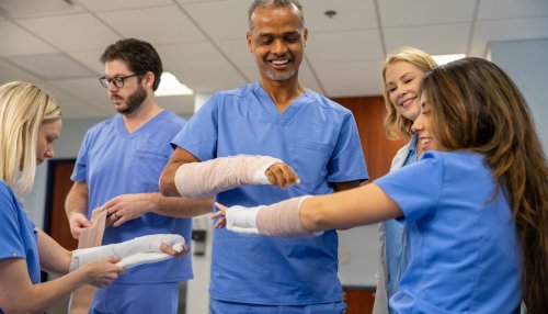Physician Assistant Studies students in scrubs practice splinting techniques on each other's arms during a clinical training session.