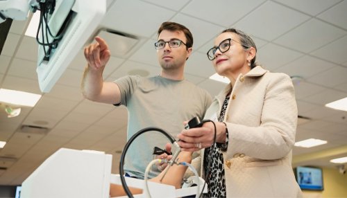 A podiatry student points to a screen while a summit participant learns to use a surgery simulator.