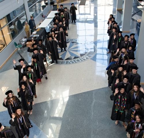 College of Pharmacy graduates stand in line while smiling and waving.