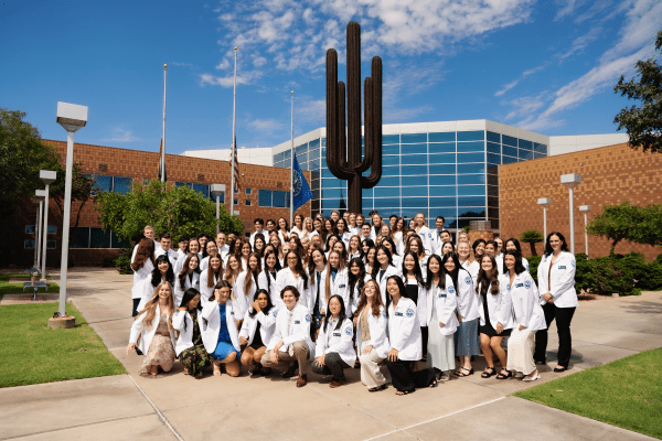 Glendale Campus first-year students wearing their white coats in front of Sahuaro Hall.