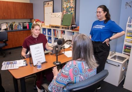 Client speaks into microphone while two students look on.