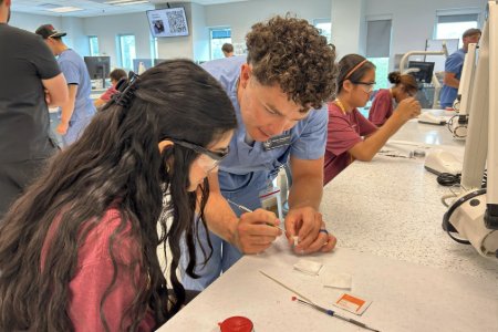 A Midwestern dental student shows a high school student how to wax a tooth in the Dental SIM Lab