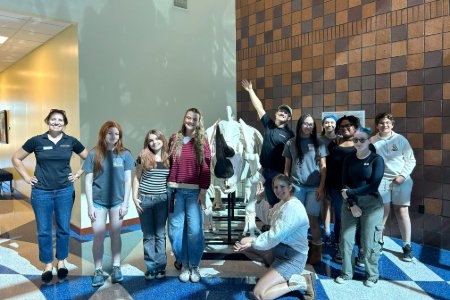 The group of teens from Phoenix Zoo Teens program pose in front of a rhino skeleton